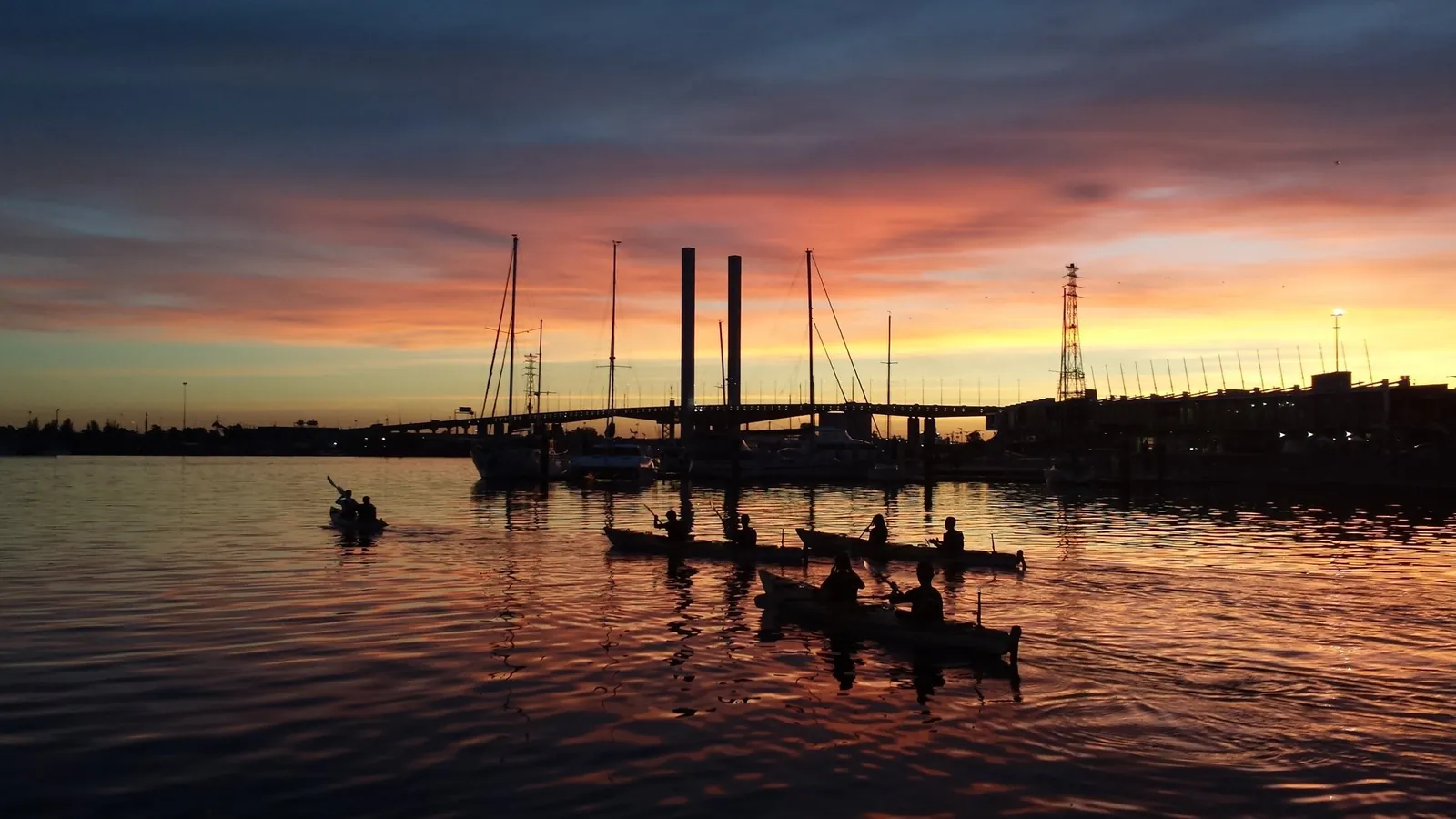 Kayaks silhouetted on calm water at sunset near the Bolte Bridge