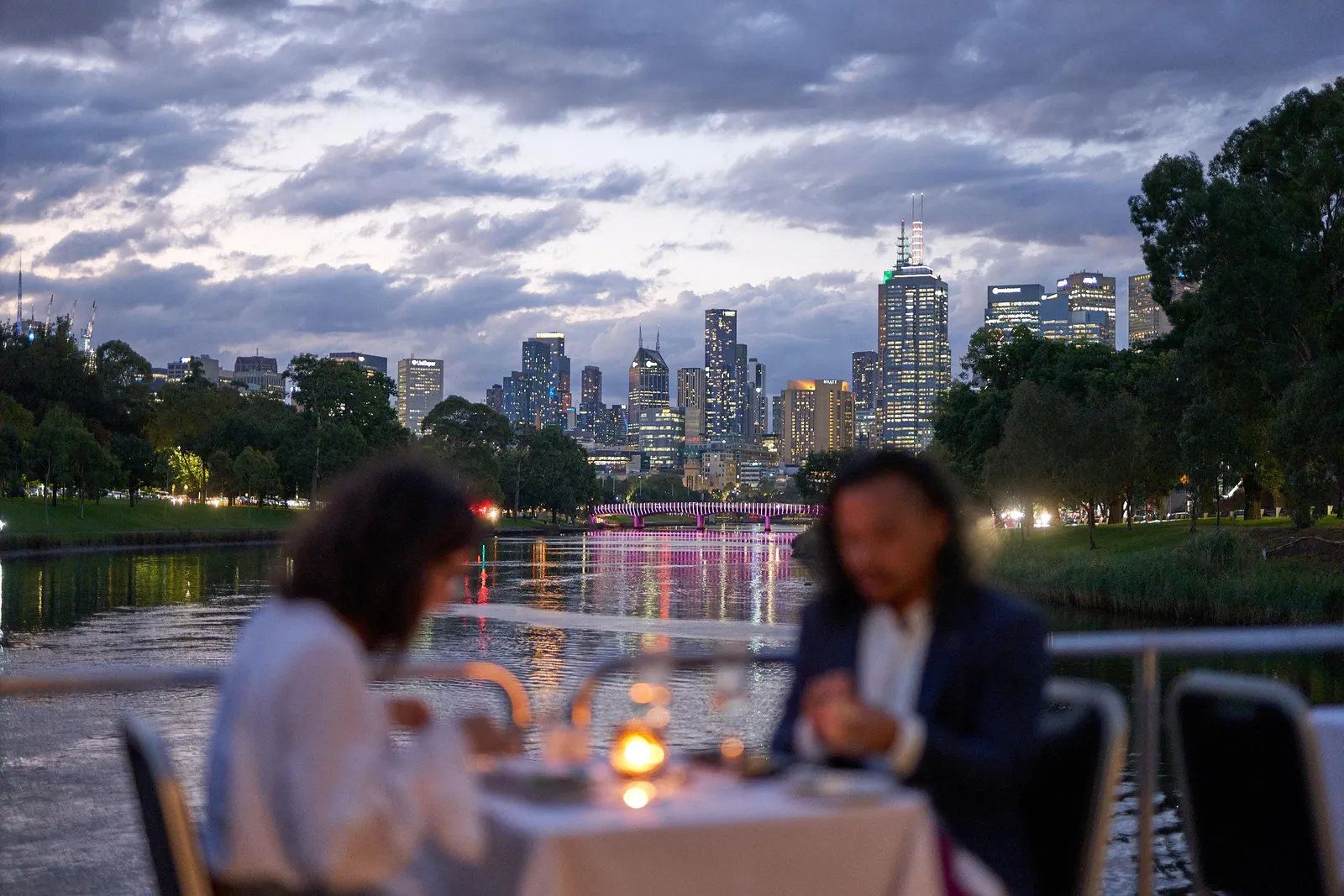 Diners at a candlelit table on a dinner cruise, the city skyline at dusk