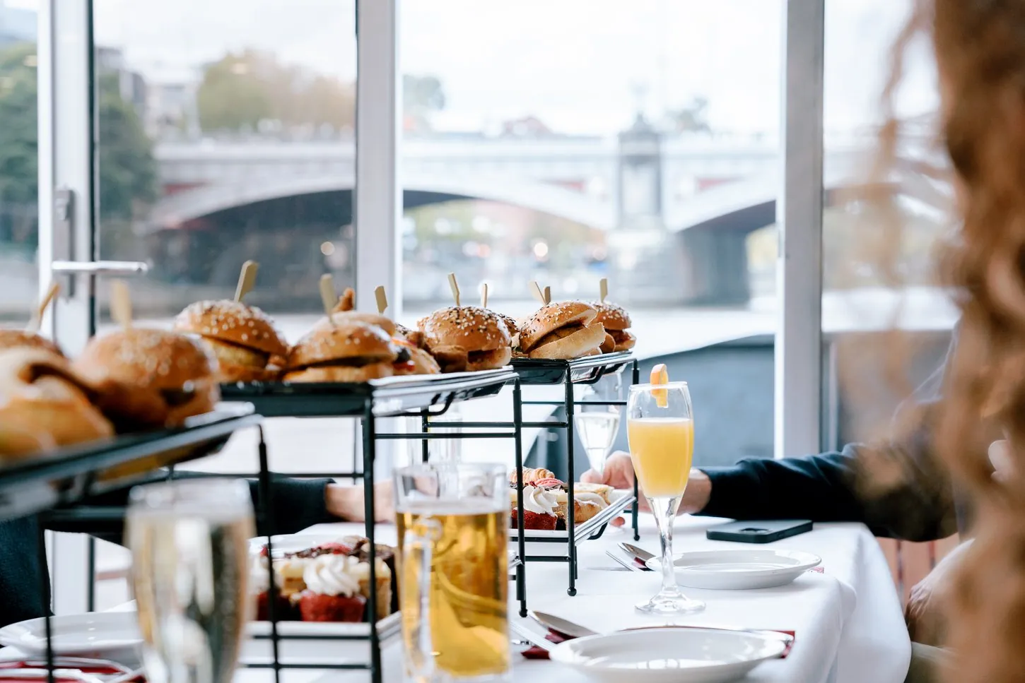 A brunch tower and drinks on a table aboard a glass-walled river cruise boat