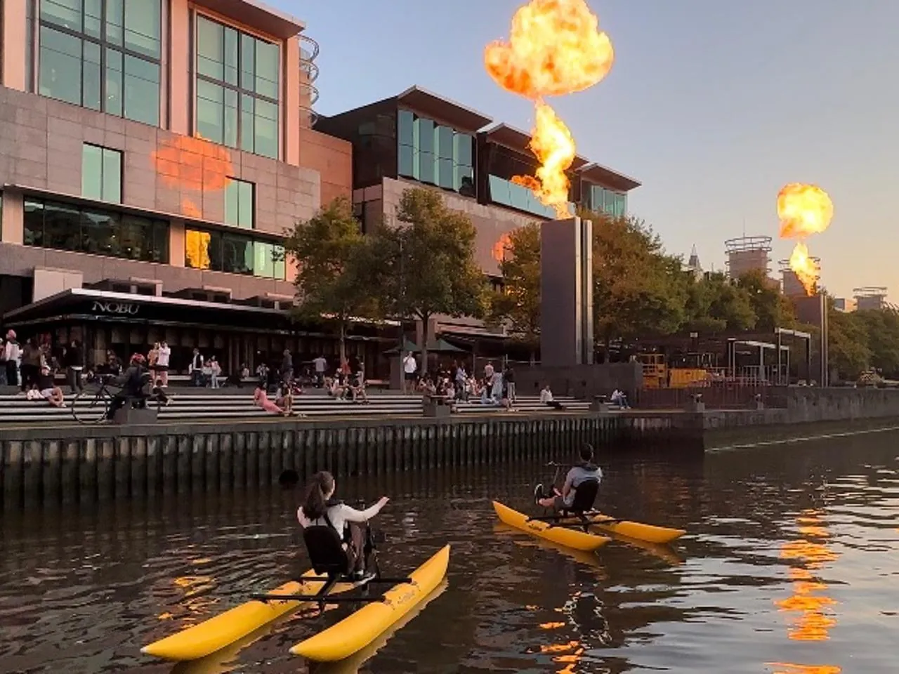 Waterbike riders on the Yarra beside the Crown fire towers at dusk