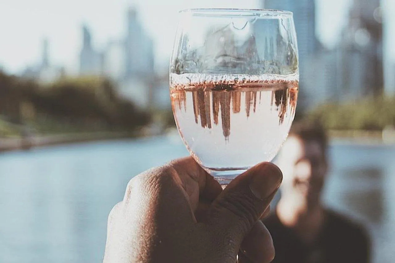 A glass of wine held up against the river and city on a sunset cruise