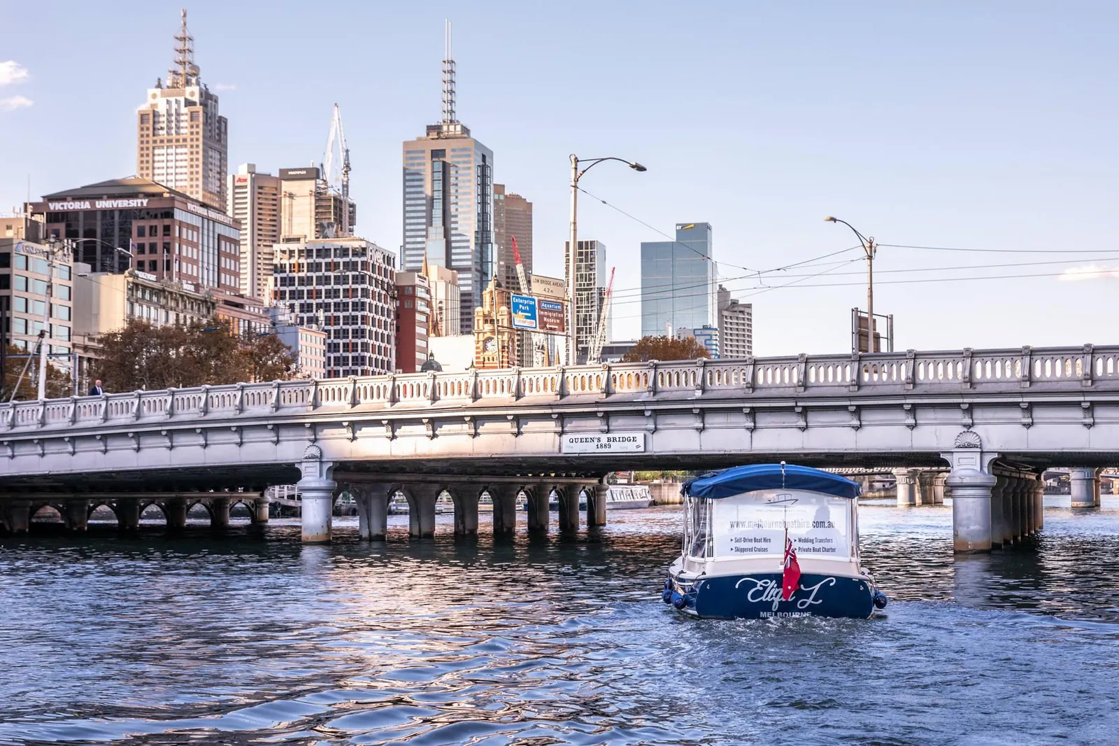 A private charter boat on the Yarra beside a stone bridge, the city skyline behind